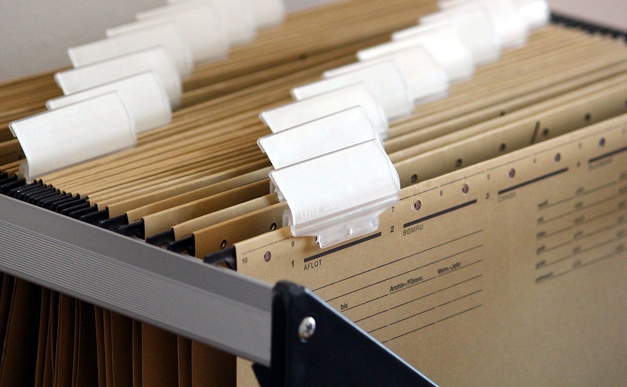 Open drawer, of a black filing cabinet, full of hanging file folders.